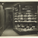 Cover image for Photograph - Adams and MacDonald cake shop Brisbane Street, Launceston, manageress Miss Gibb in doorway. Harold Andrew photograph. [Next to Metropole Hotel.]