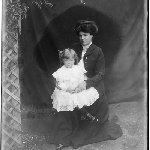 Cover image for Photograph - Woman posing for photograph with child in white dress on her lap