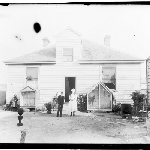 Cover image for Photograph - Rear view of weatherboard house  [showing avaries, people and garden]