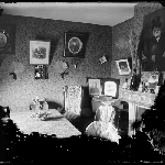 Cover image for Photograph - Interior parlour/sitiing room [portraits on wallpapered wall showing items on mantlepiece]