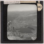 Cover image for Photograph - Two climbers on a mountain top overlooking a mountain lake (Probably Lake Rodway, the Little Valley (with tarn at the end) and the base of Mount Emmett from Cradle Mountain) / Fred Smithies [lantern slide]