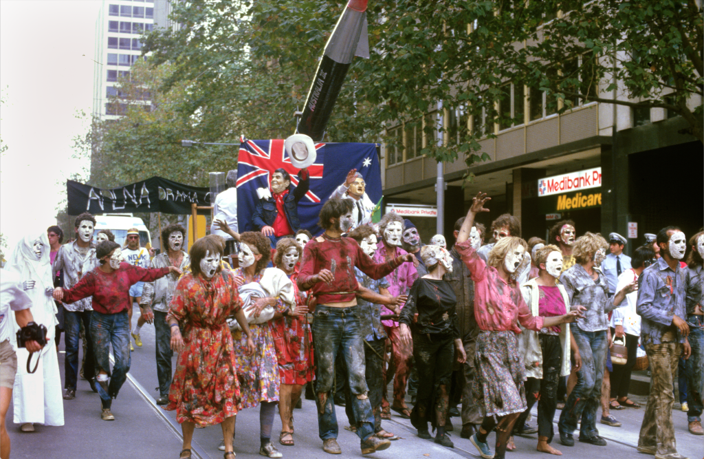 A colourful group of people with masks on protesting against nuclear energy in a Melbourne city street.