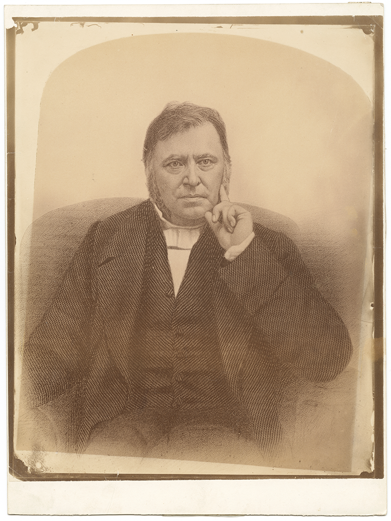 Portrait of John West, a middle-aged man with sideburns, wearing a dark suit and white cravat. He sits with his right hand near his face, index finger resting on his cheek