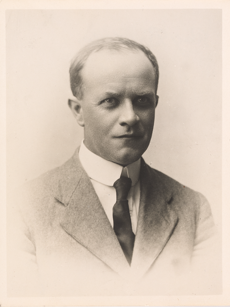 Portrait of Roy Bridges, a middle aged, blading man in a suit and tie.