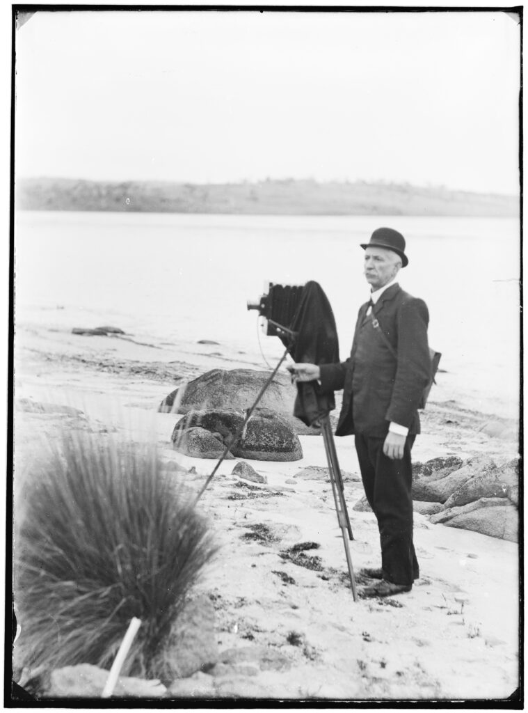 A man in a suit on the beach with an old style camera on a tripod