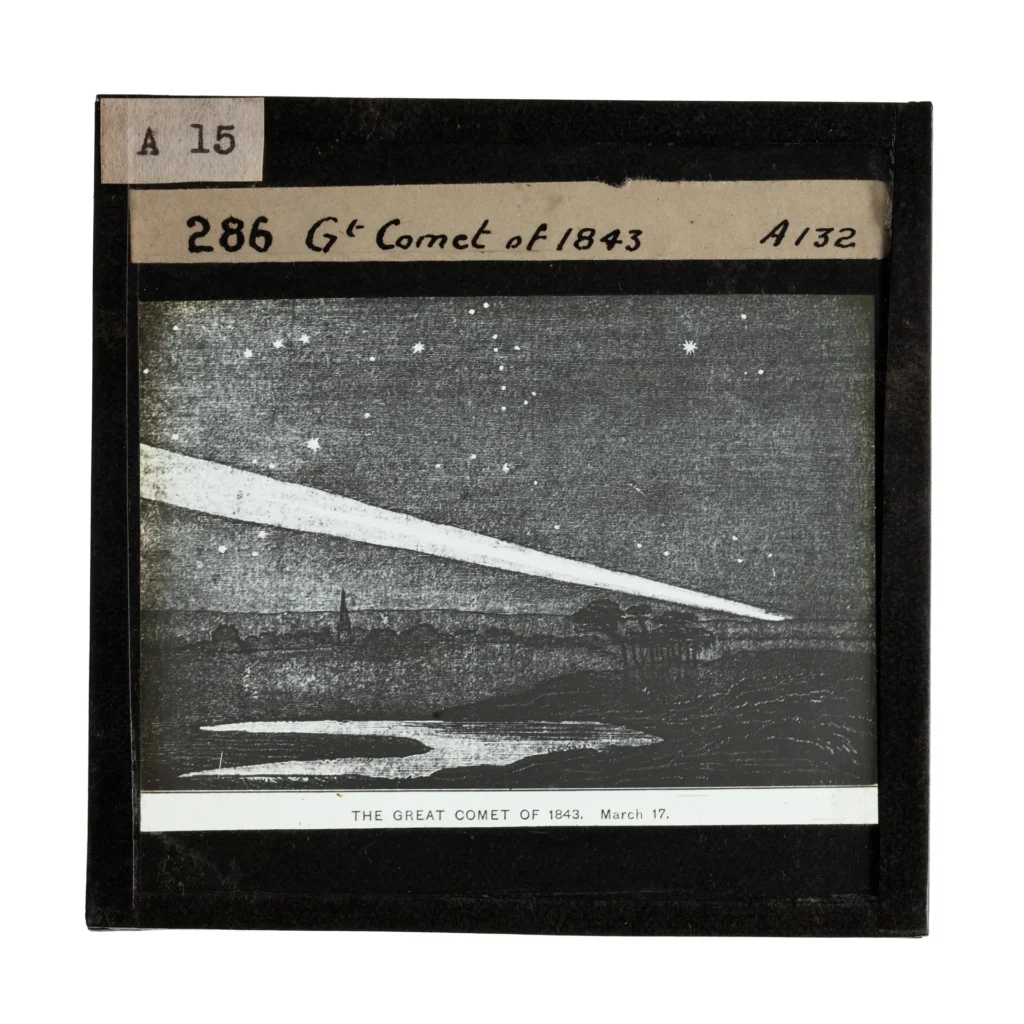 photograph of a glass lantern slide depicting a black and white engraving of a comet blazing across a starry night sky. There is a lake in the foreground and the silhouette of trees and a chuch spire