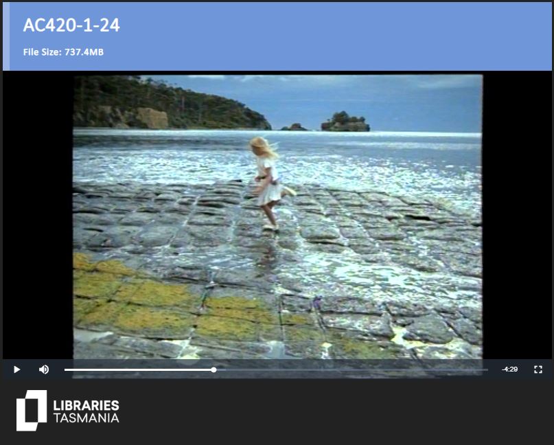 A still image from an old film. A girl walks along stons next to the ocean. Text at the top reads: "Ac420-1-24. File Size: 7.37.4MB"