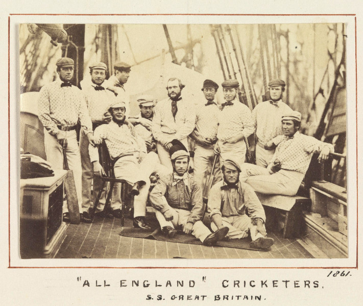 A black and white photo of 12 men in cricketer uniforms posing for a photo on the deck of a sailing ship.