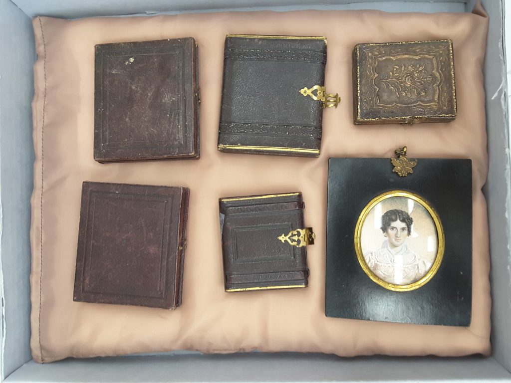 A box containing portaits with covers on them, one is uncovered and contains a portrait of a woman in a white dress.