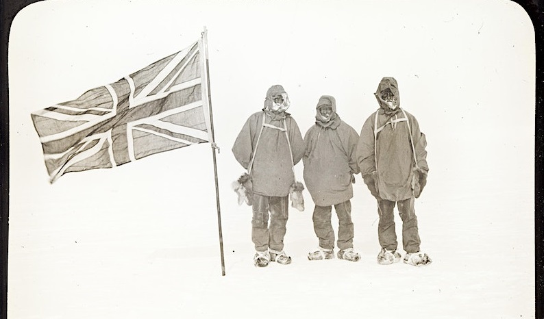 There people cover winter PPE stand next to a Union Jack Flag in Antarctica