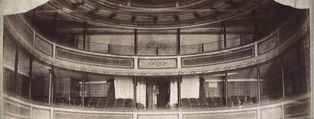 A black and white photo of the upper level of a theatre seating as seen form 