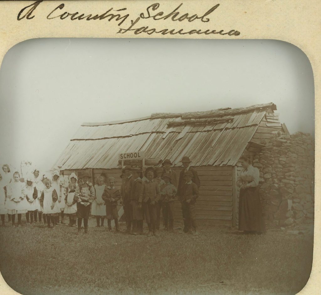 An old black and white photo of children outside an old school. Title text at the top reads: " A country school Tasmania."