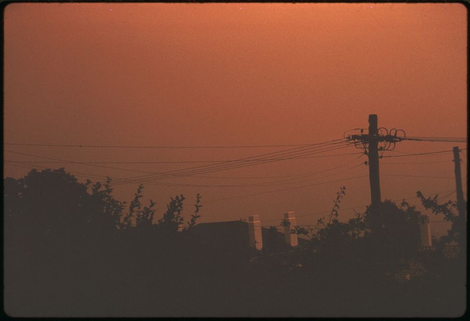 A picture of a house and power lines with a Smokey red sky.
