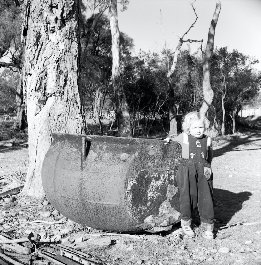 A black and white photo of a girl standing next to a cauldron.