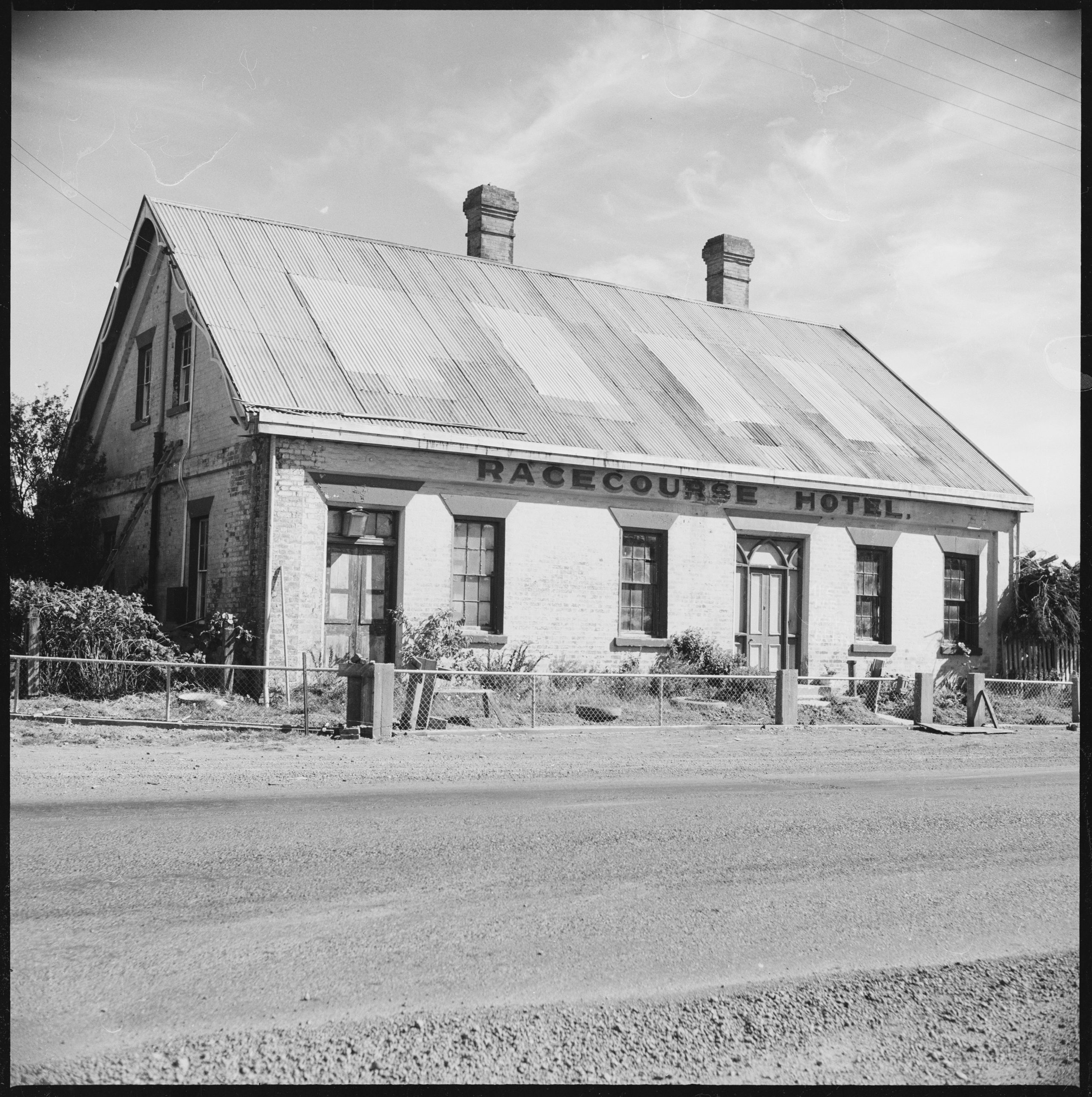 An old black and white photo of a motel seen from the road. Text on the hotel reads: "Racecourse Motel"