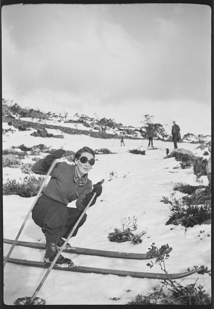 An old black and white photo of a skier sliding sideways on mount wellington with 3 people standing in the background