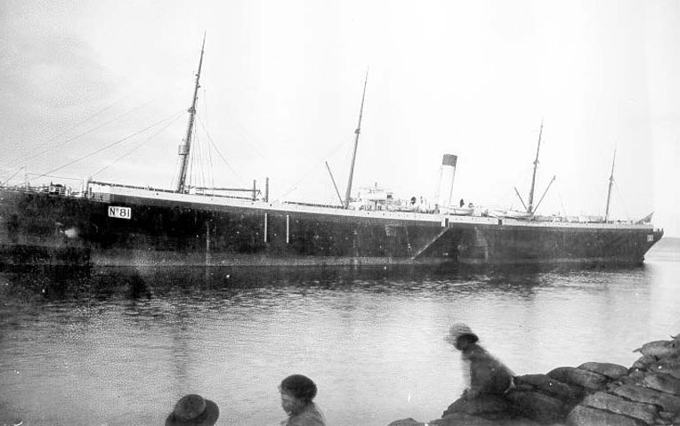 A black and white photo of a long ship on the water.