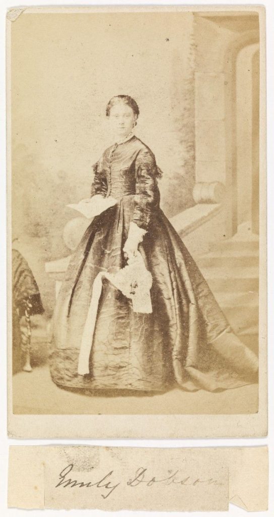 An old black and white photo of a woman, Emily Dobson in a dress. posing for a photo.