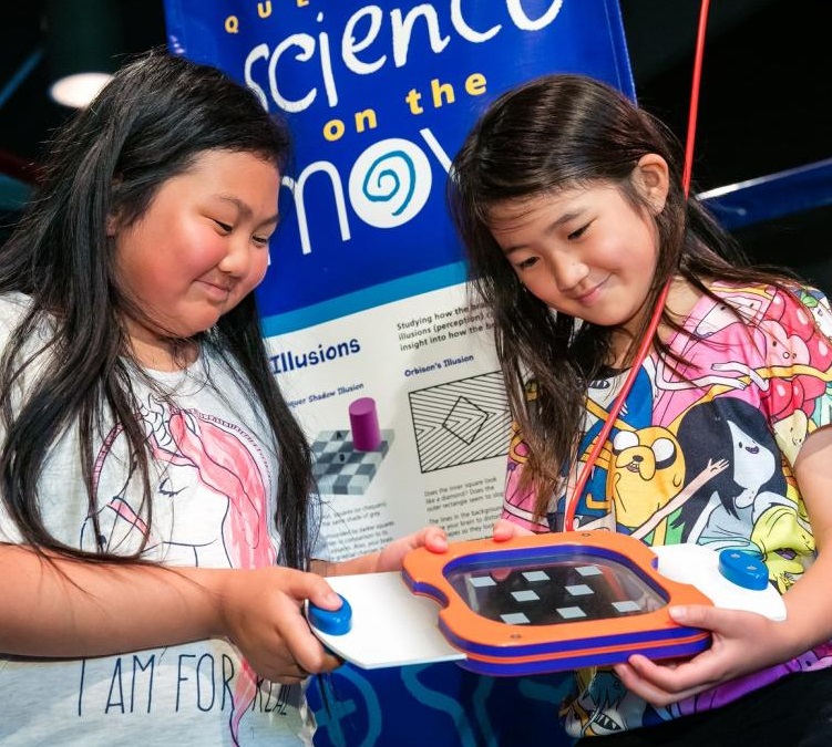 Two girls looking at a device in front of a poster.