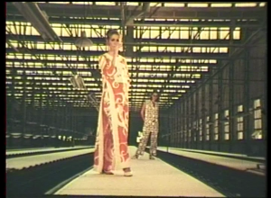 a still taken from Film – The Other Face Of The Island (1970). A woman standing in a warehouse